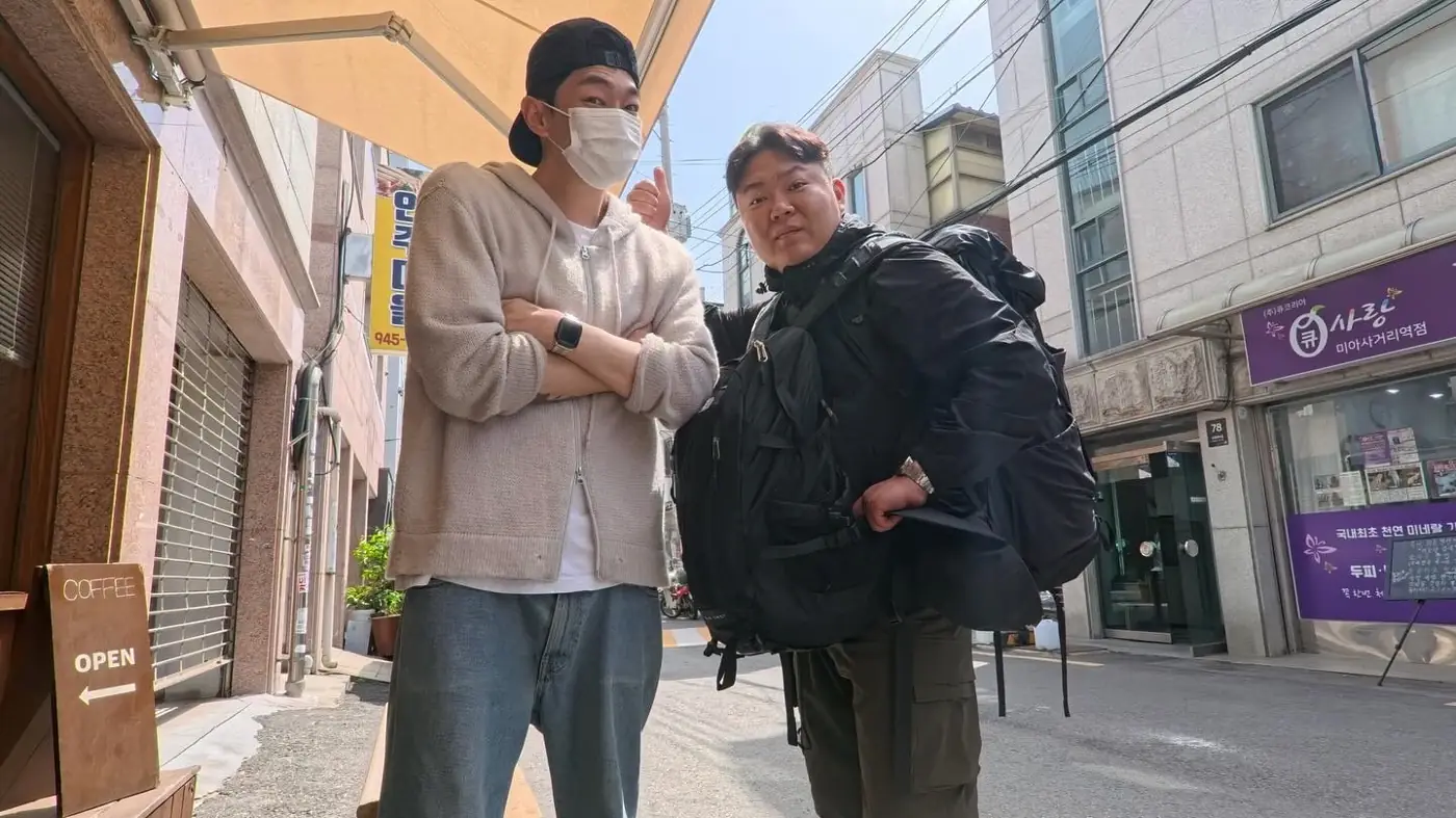 배낭을 멘 두 사람이 서울 골목에 서 있다