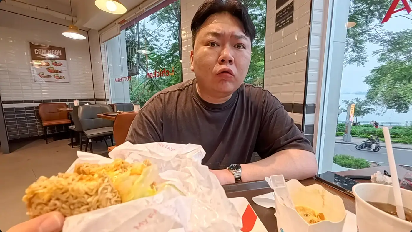 튀긴 라면을 빵 대신 쓴 버거를 들고 앉아 있는 모습