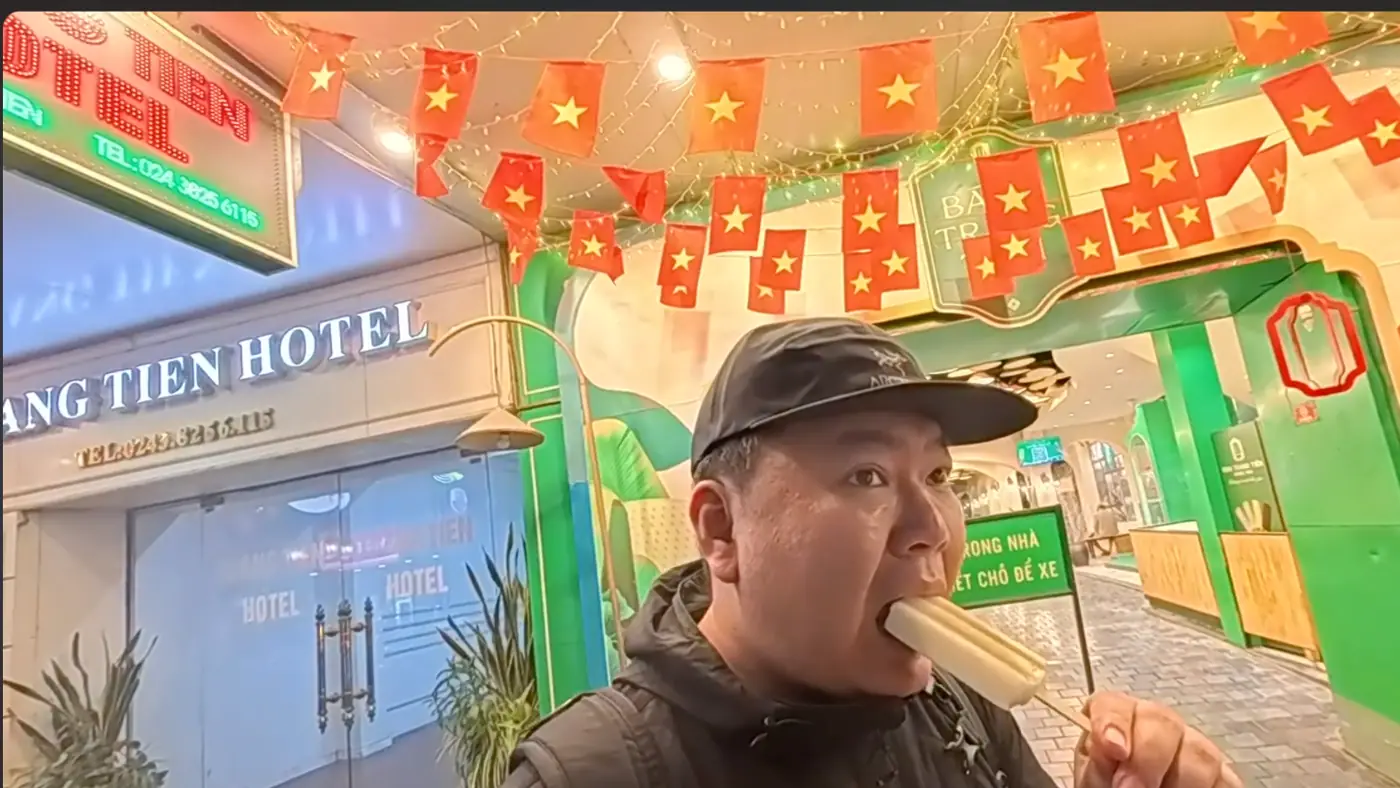베트남 국기가 걸린 가게 앞에서 하얀 막대 아이스크림을 먹는 모습