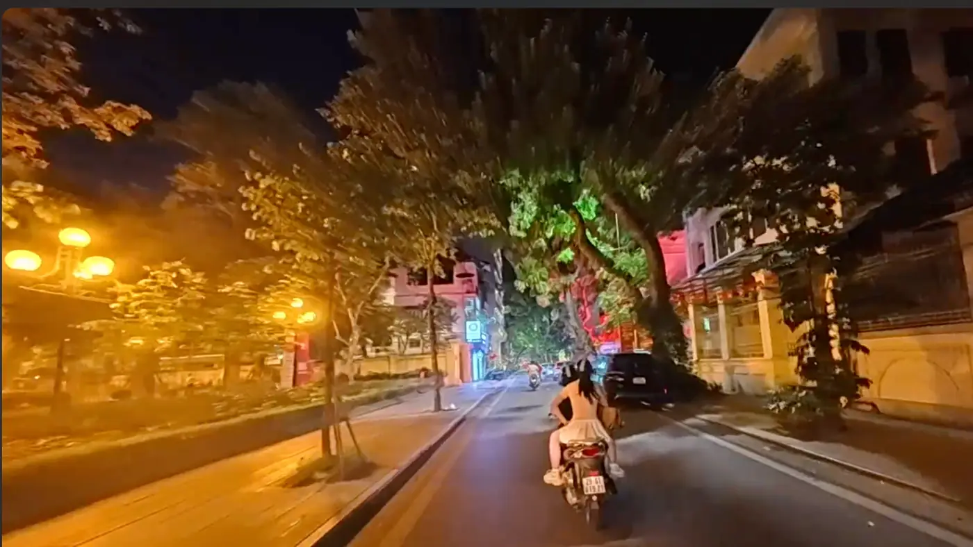가로등과 나무가 이어진 하노이 밤길을 달리는 오토바이