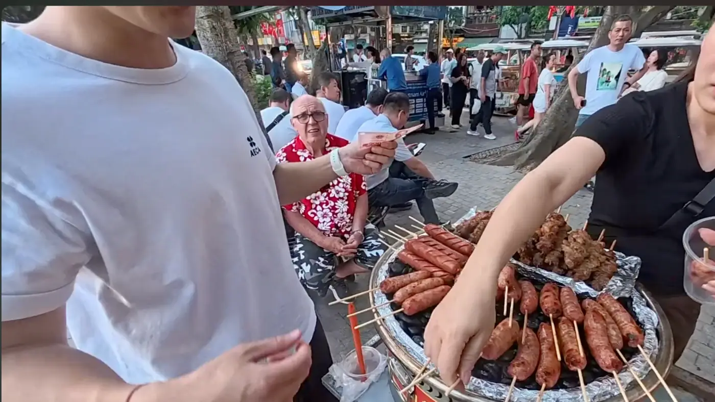 숯불 위에 줄지어 놓인 소시지 꼬치와 지폐를 내미는 손