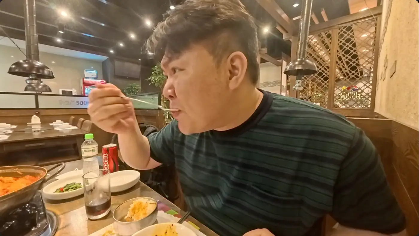 한식당 안에서 숟가락으로 부대찌개를 떠먹는 모습